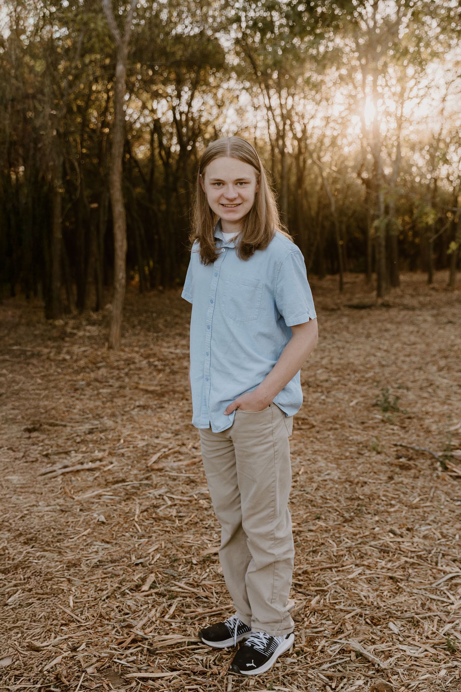 A casual outdoor portrait in a wooded area at sunset with golden light filtering through the trees.