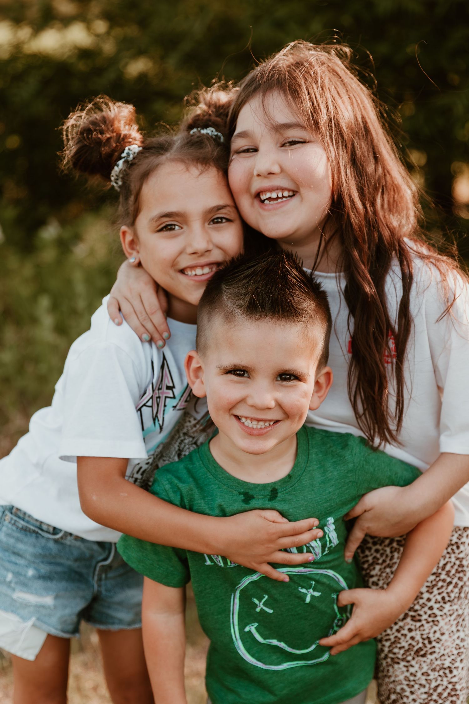 Sweet siblings embrace and laugh together while wearing casual summer outfits in golden outdoor lighting.