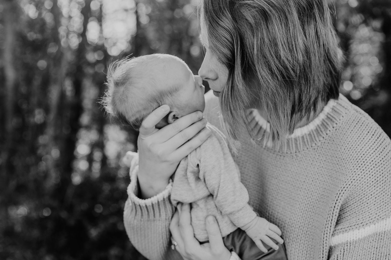 A tender black and white moment between parent and baby outdoors in a wooded setting.