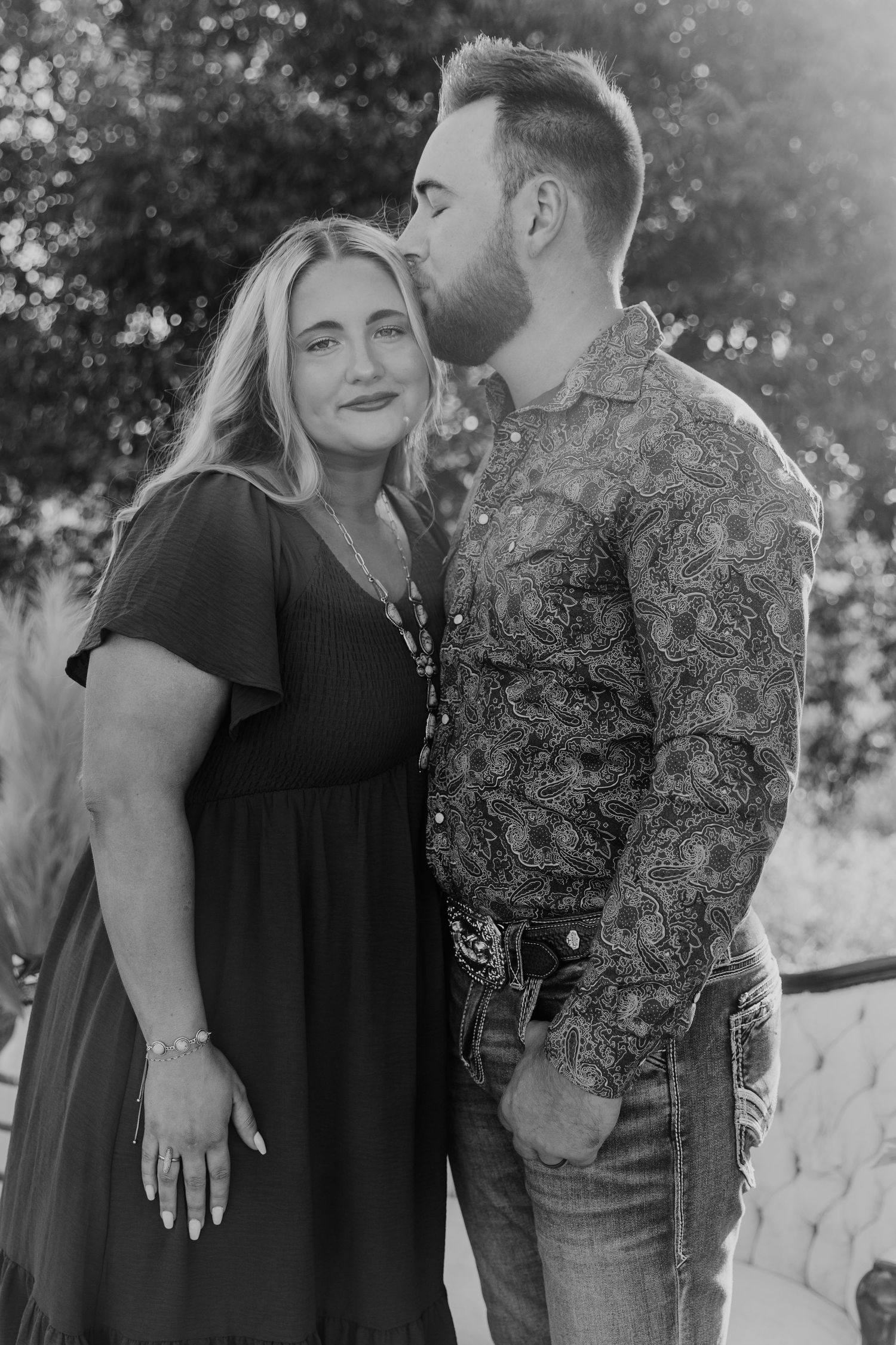 A couple shares an intimate moment on a vintage couch outdoors wearing black and floral prints.