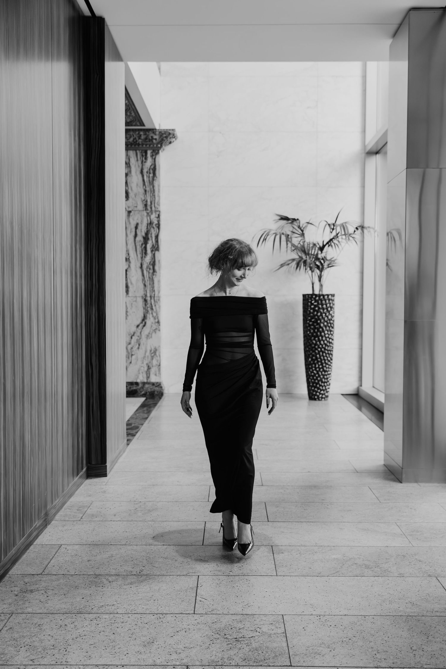 A black and white series of four photos showing a figure in dark clothing walking away down a minimalist hallway.