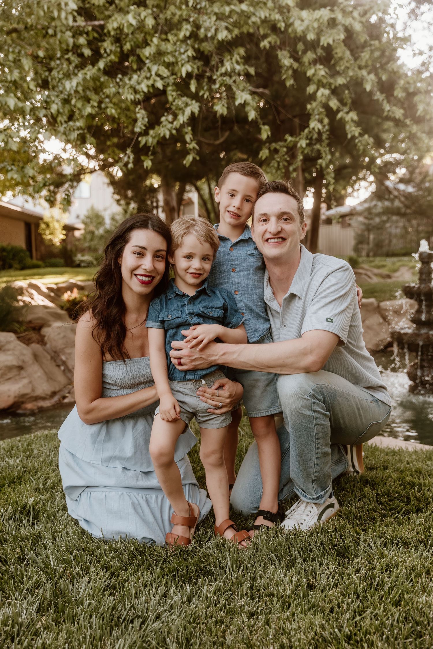 Happy family of four posing together on green grass in a backyard garden setting.