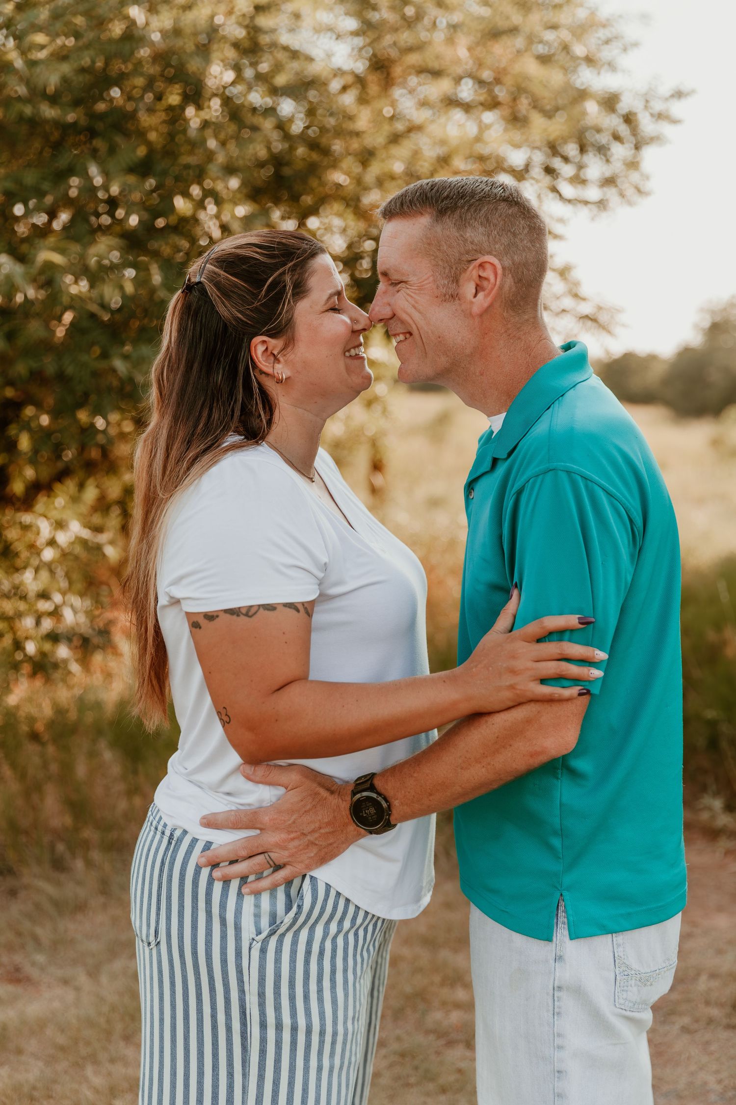 Romantic couple embraces outdoors at sunset with golden light and autumn trees in background.