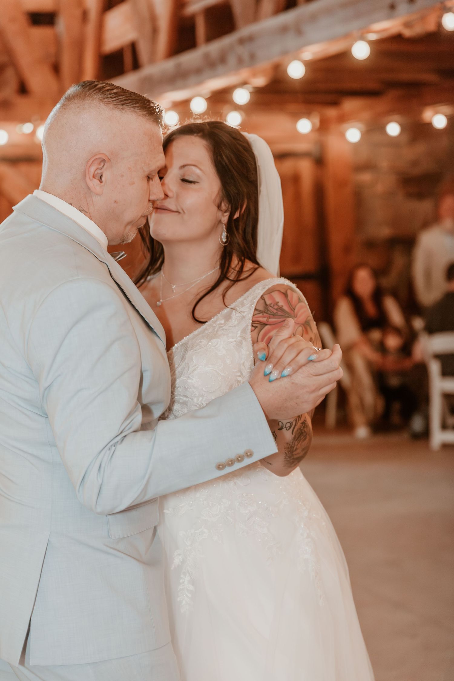 A romantic newlywed couple share an intimate dance moment at their reception with string lights glowing in the background.
