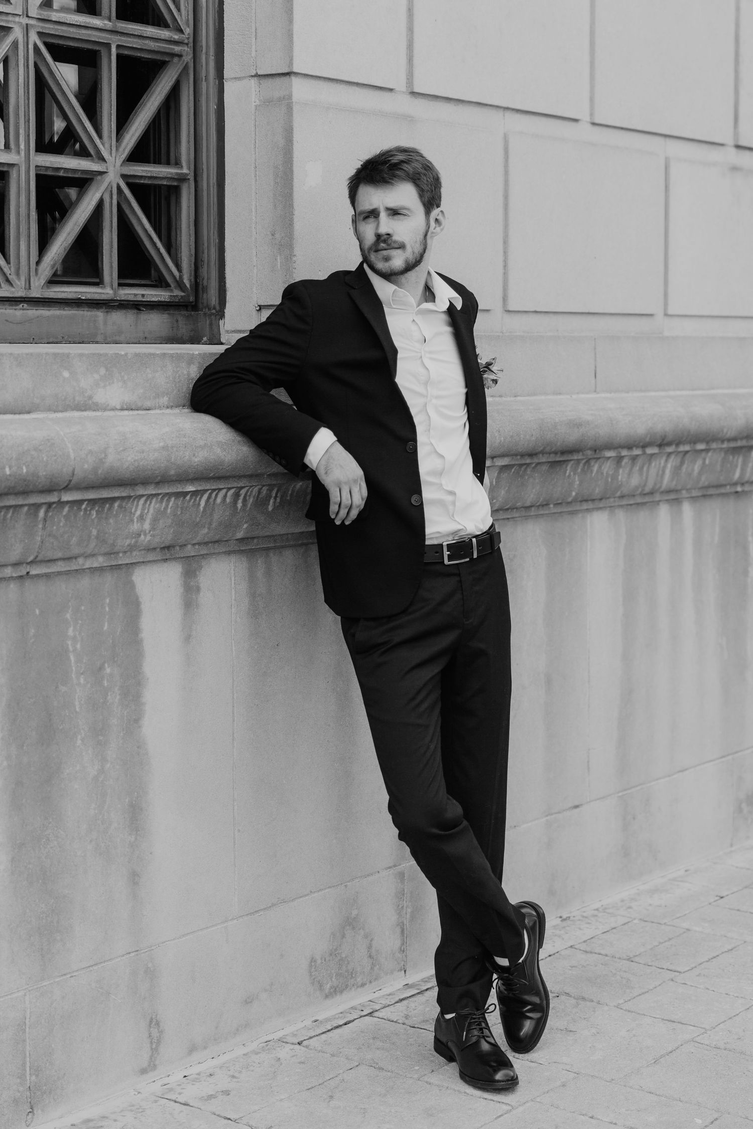 Black and white photo series showing a person in formal attire striking dramatic poses against a stone building wall.