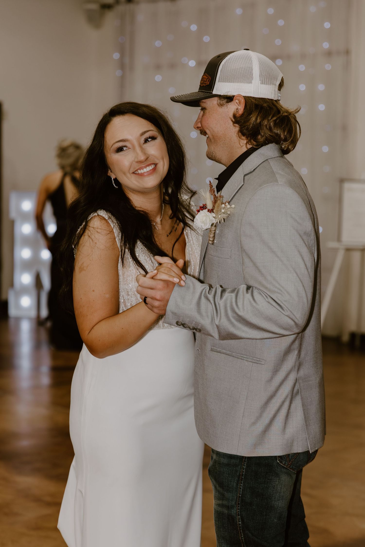 A couple shares their first dance at their wedding reception with twinkle lights in the background.
