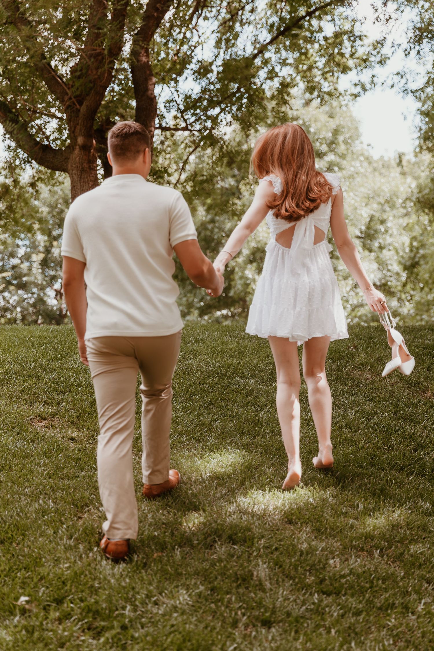 Two people walking up a grassy hill in coordinated white and beige outfits on a sunny day.