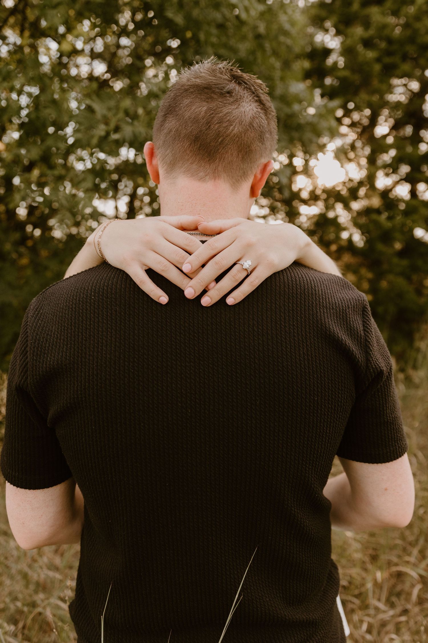 Hands gently embrace around shoulders in an intimate back view portrait outdoors.