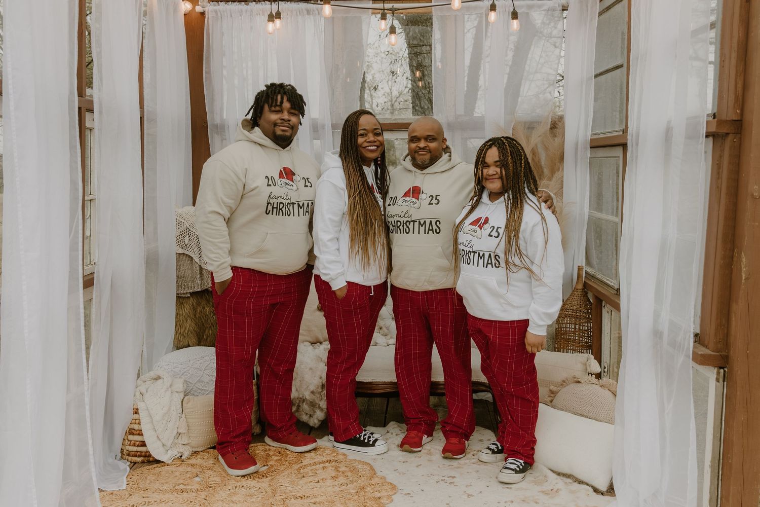 Four people wearing matching white sweatshirts and red pants stand together against a light colored backdrop.