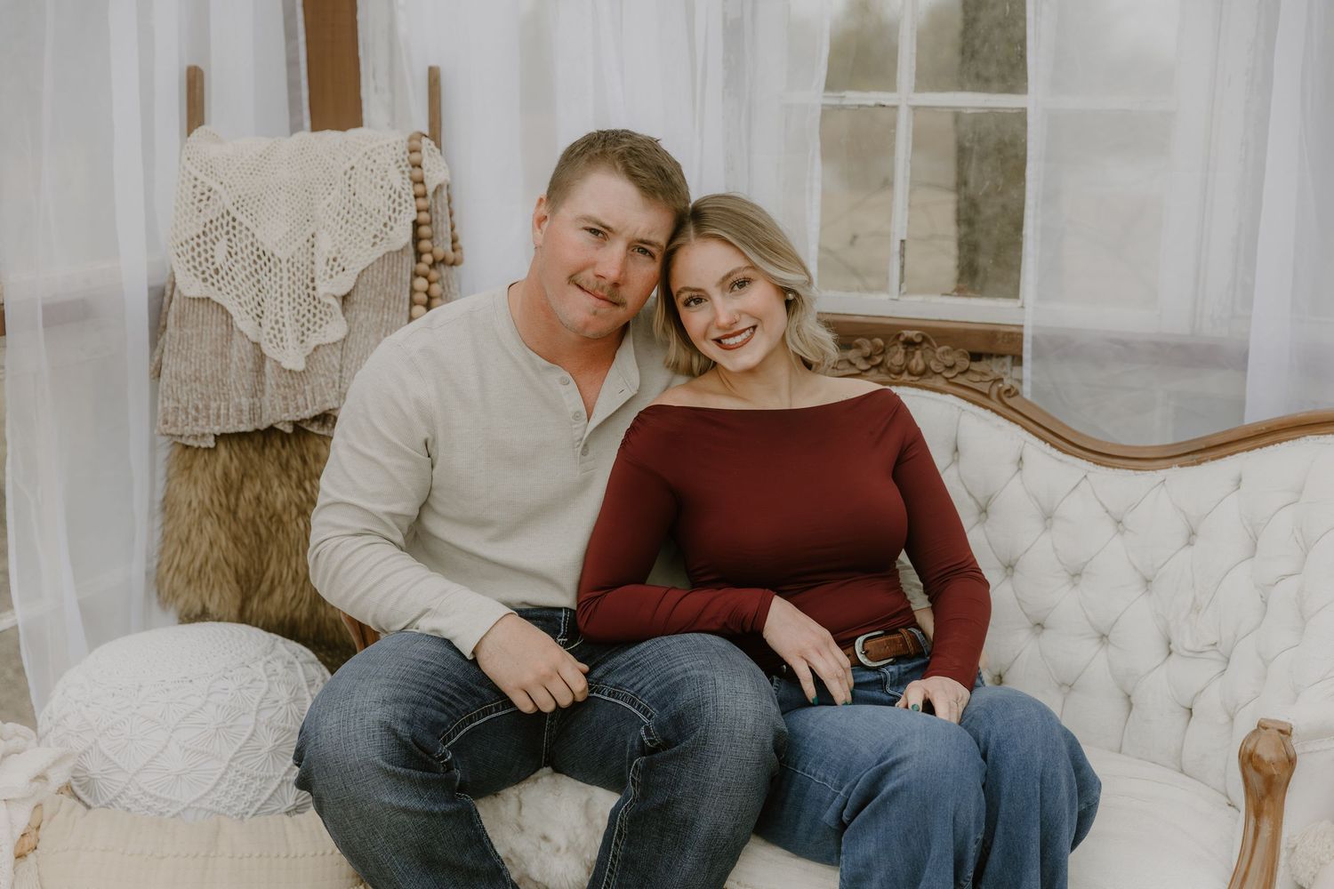 Couple sitting together on elegant white tufted sofa in romantic indoor photoshoot setting.