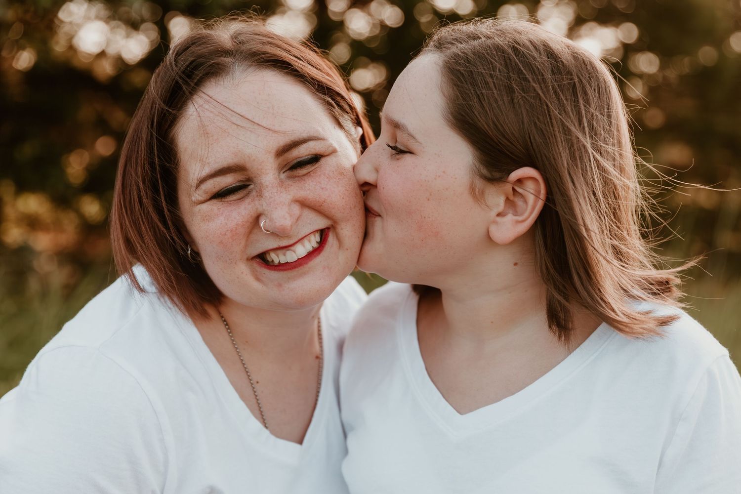 Two people in white shirts share a joyful candid moment outdoors with warm golden lighting in the background.
