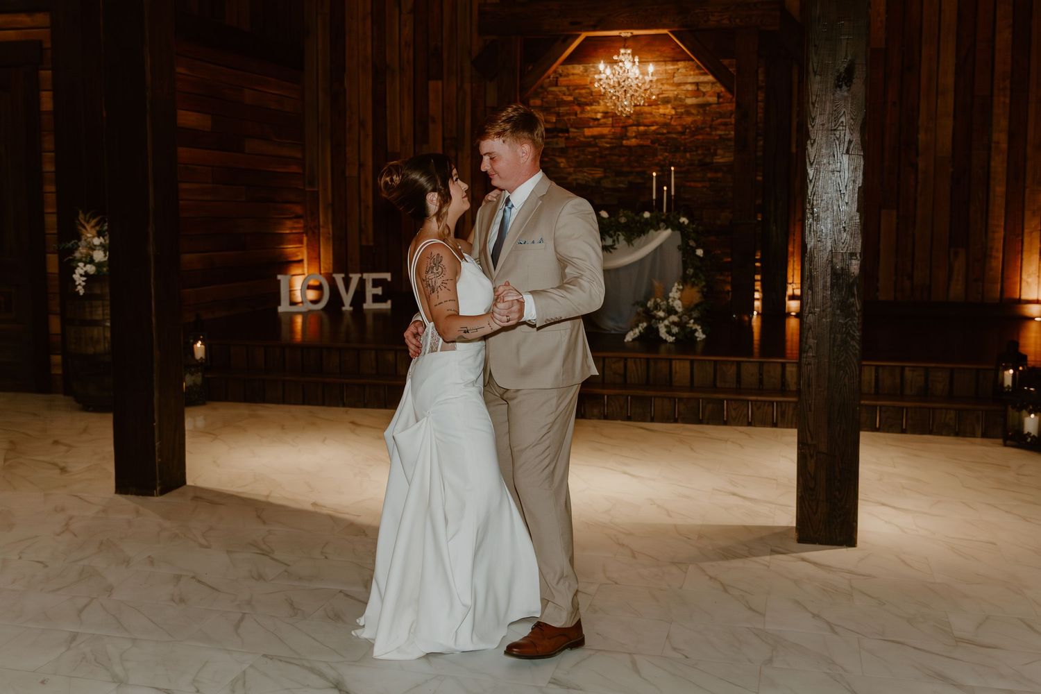 A couple dances together during a romantic evening wedding celebration in a rustic wooden barn venue.
