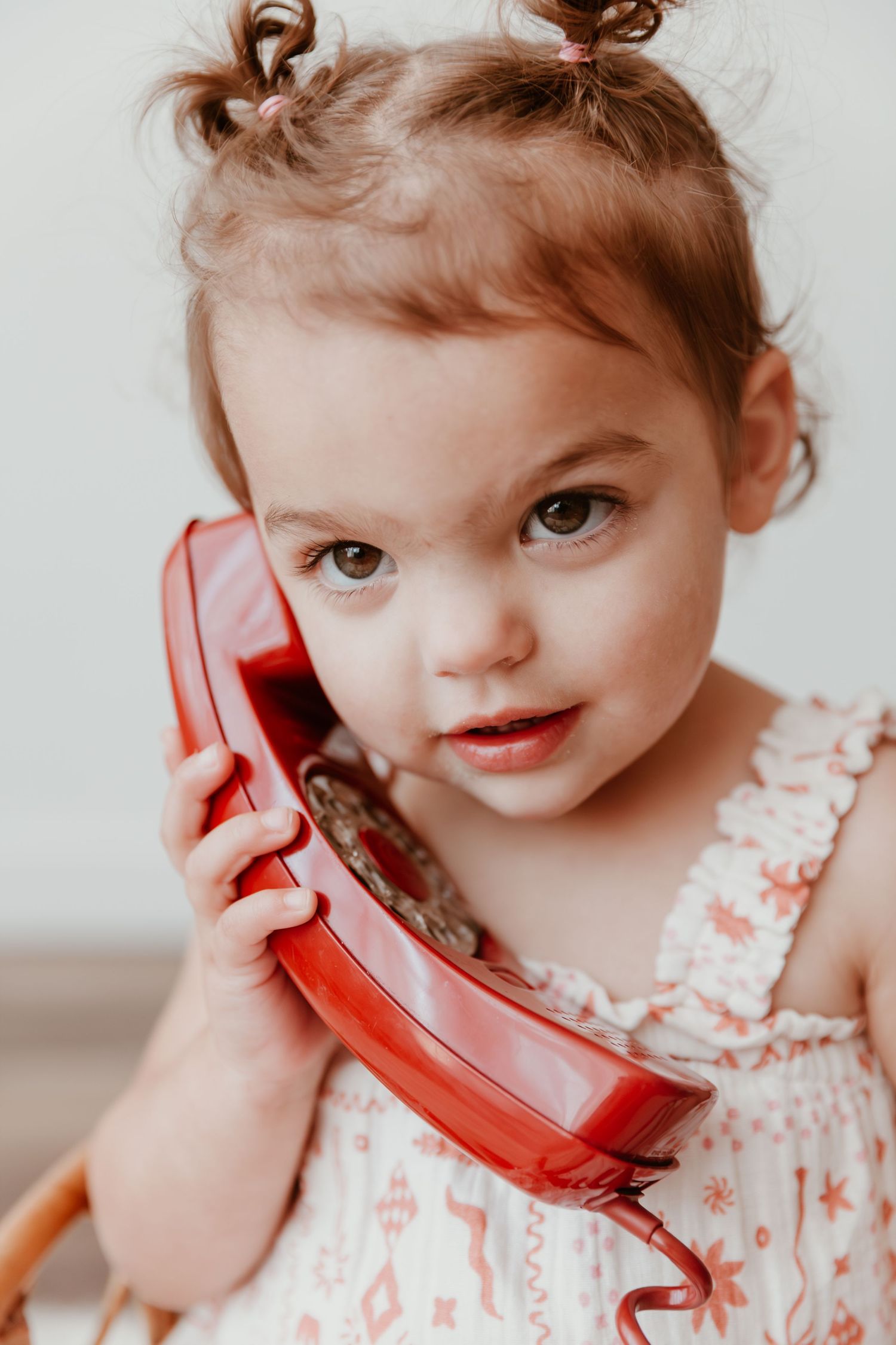 A child in a floral dress holds a vintage red rotary telephone receiver making a series of playful expressions.