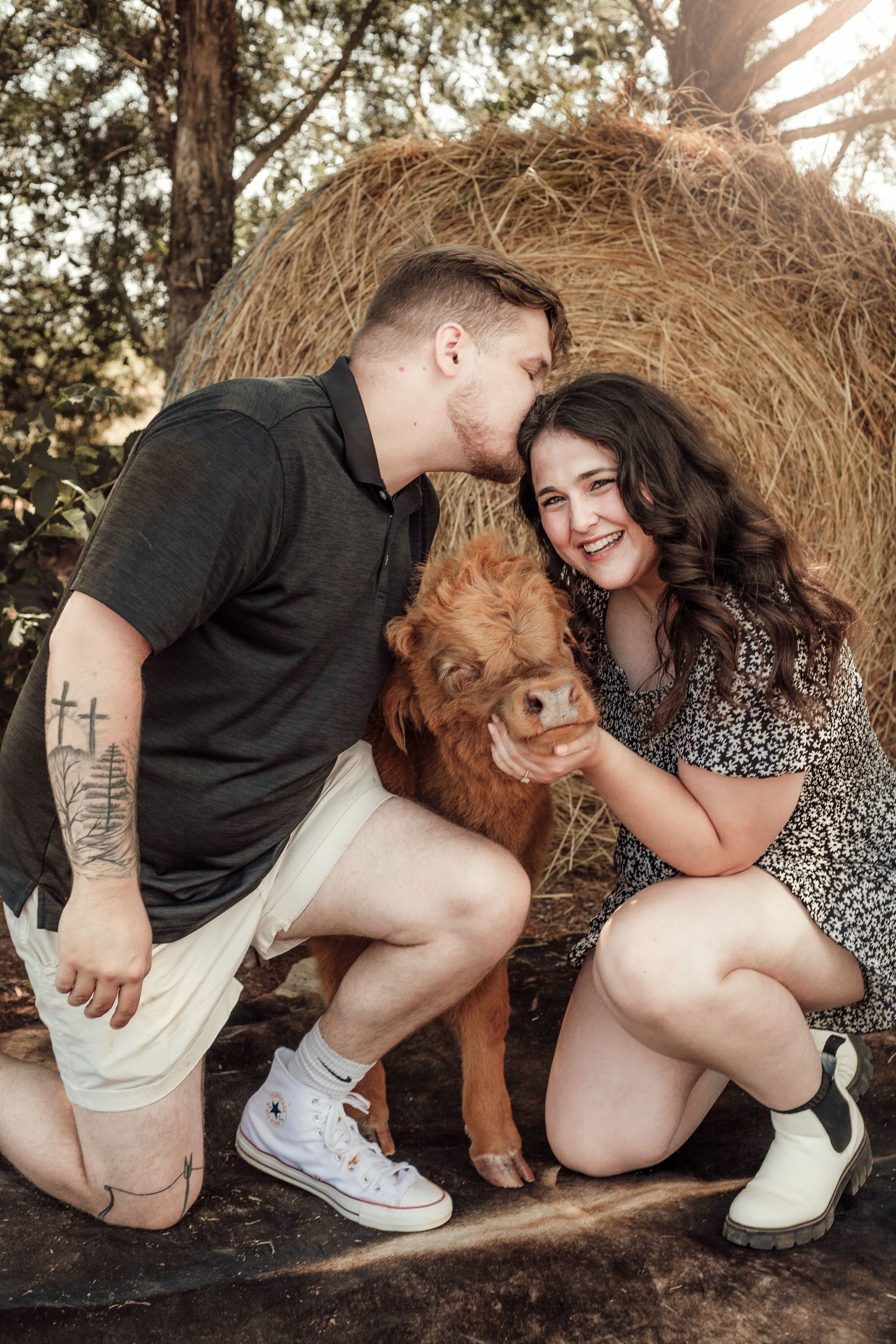 A couple poses with their golden retriever by a large hay bale during an engagement shoot.