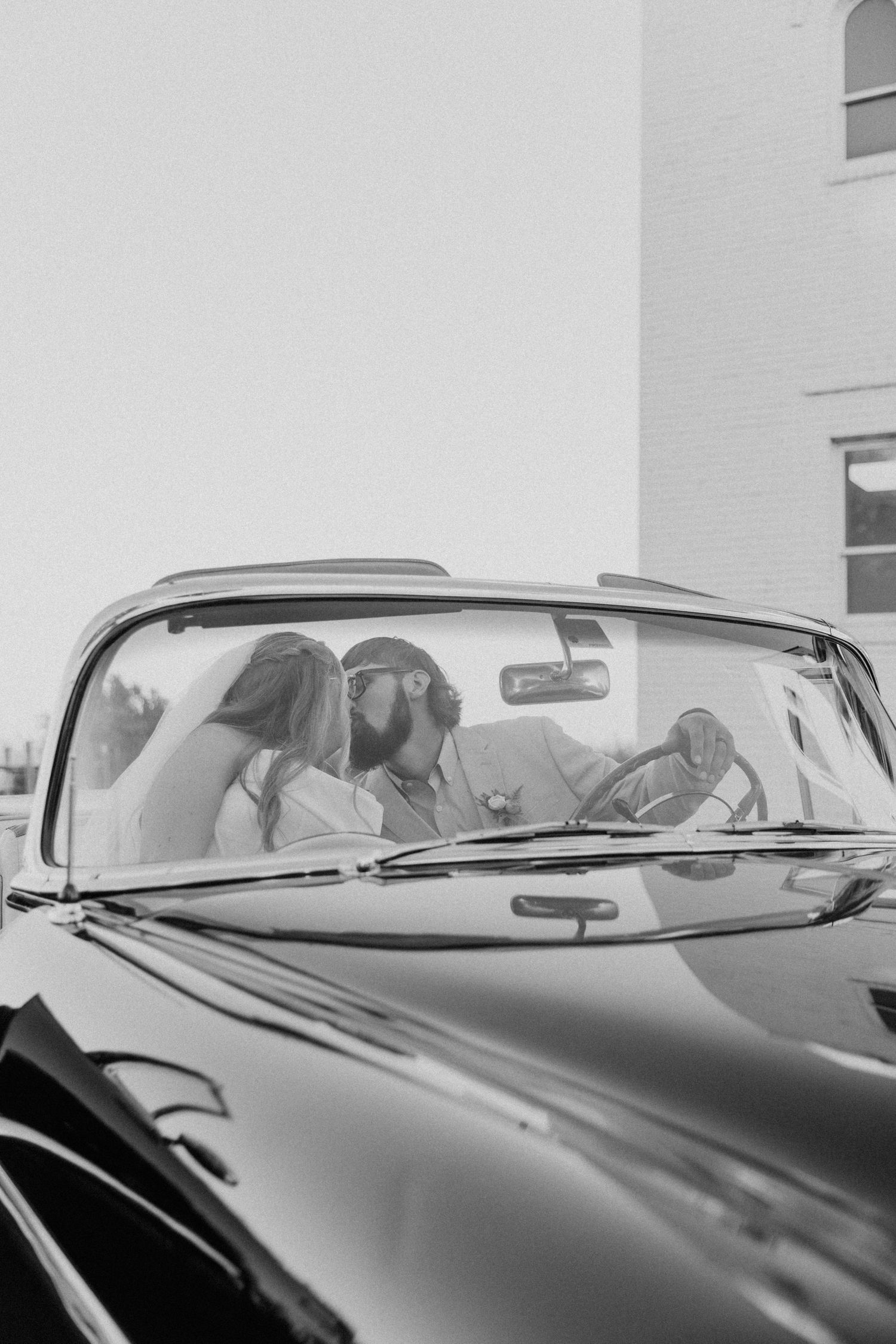 Vintage cars lined up in a row showing their sleek black hoods and chrome details in black and white.