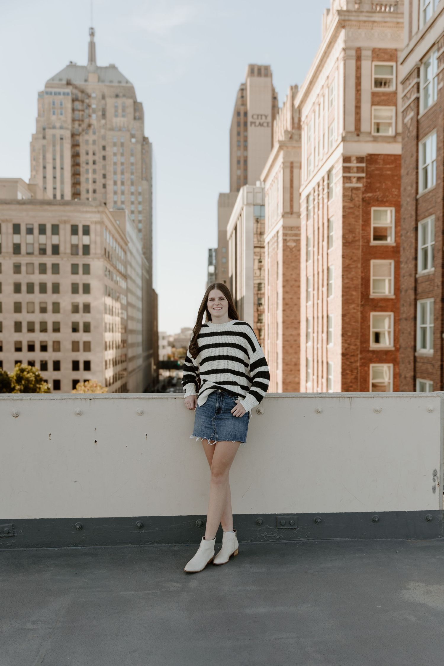 A person in a black and white striped sweater poses on a rooftop with historic brick buildings visible in the cityscape.