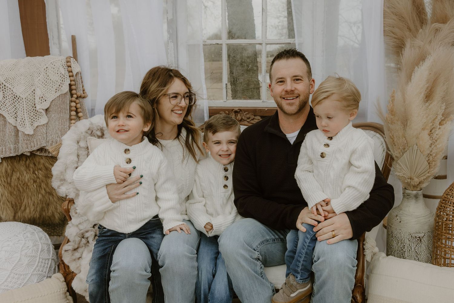 A family of five wearing coordinated white and black outfits sits together on a couch for a casual indoor portrait.