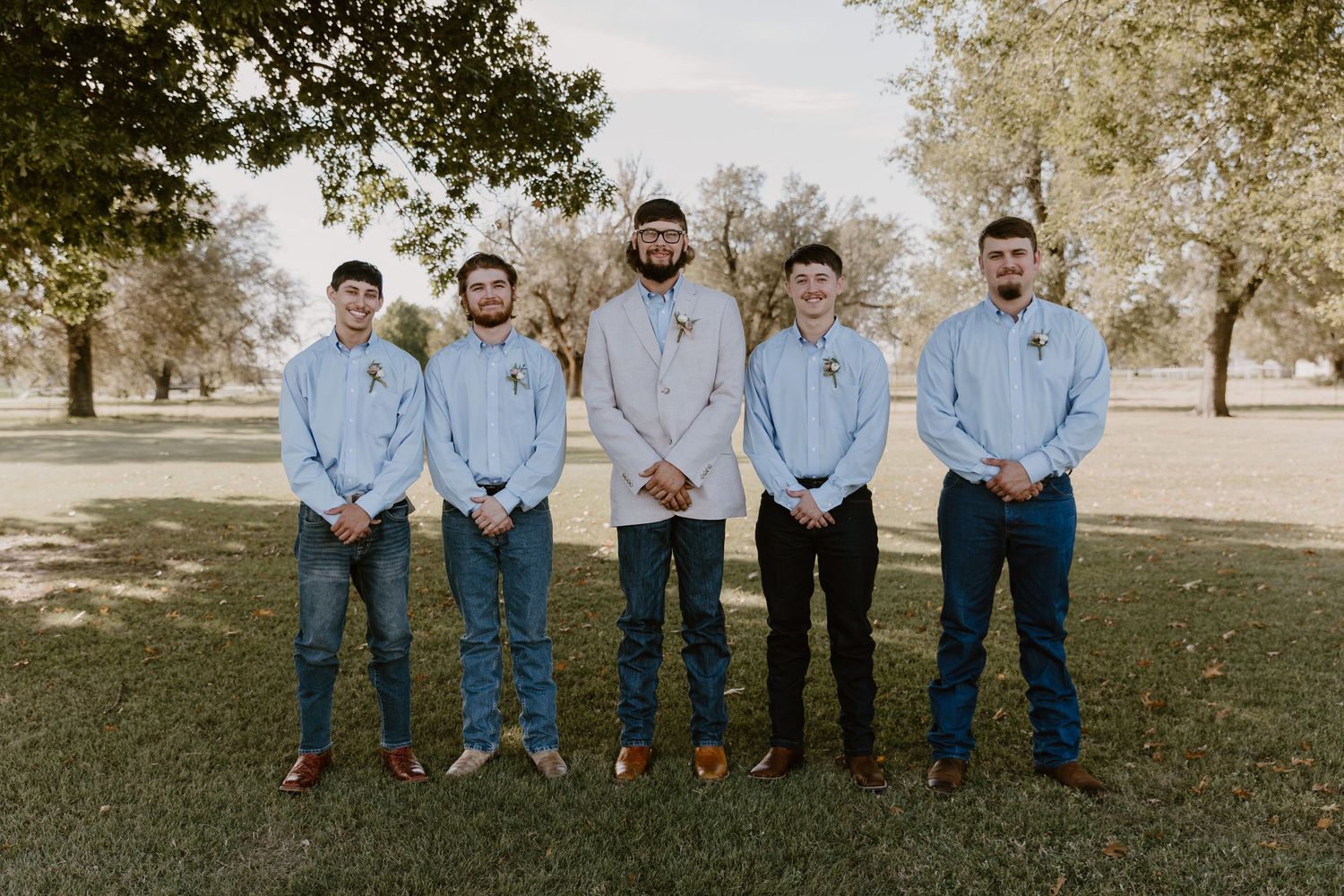 A group wearing matching light blue shirts and jeans pose together on grass in a casual outdoor setting.