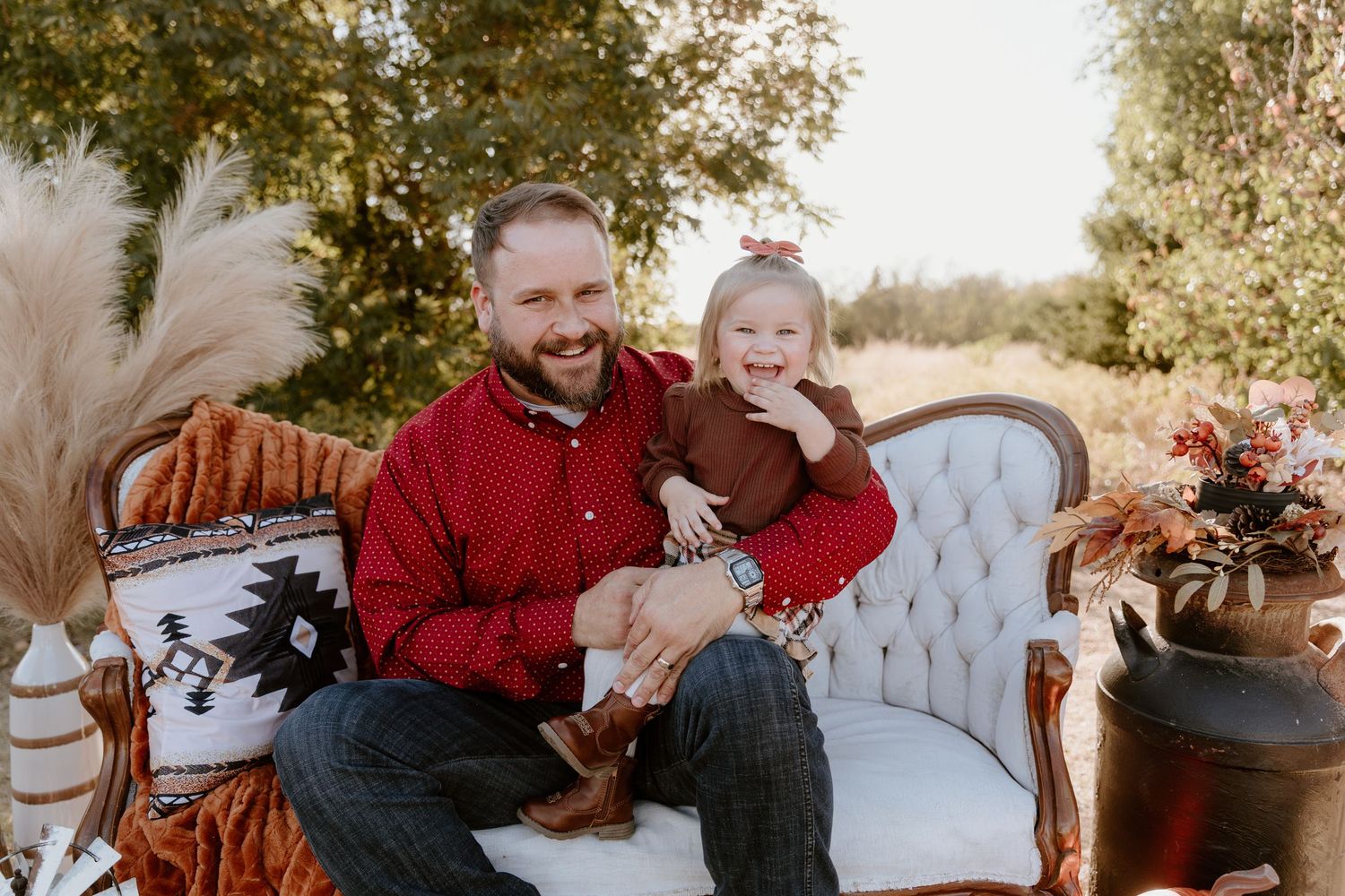 Family wearing red and grey outfits poses together in outdoor autumn setting during golden hour.
