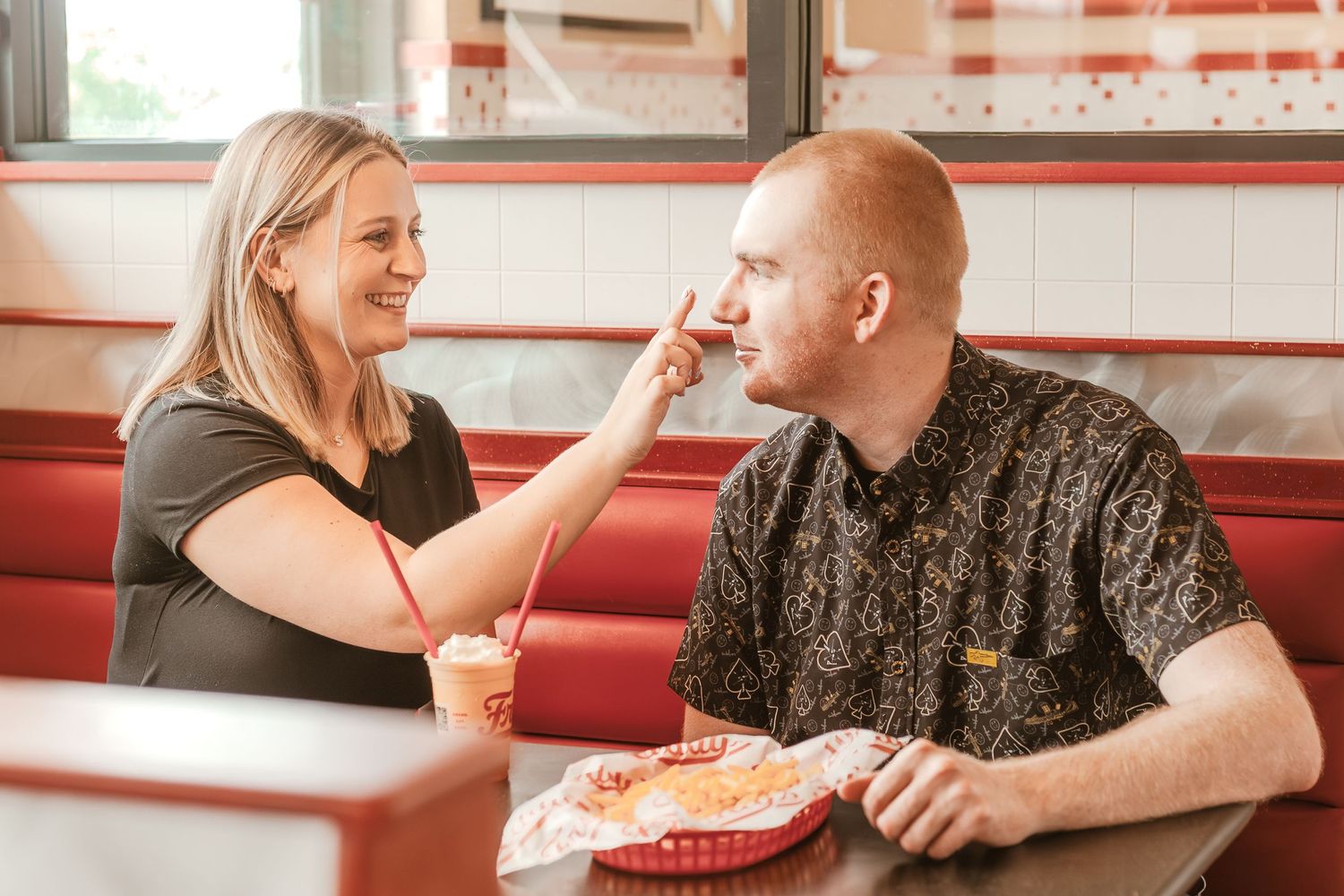 A playful dining scene as a couple shares food and laughter in a restaurant booth.