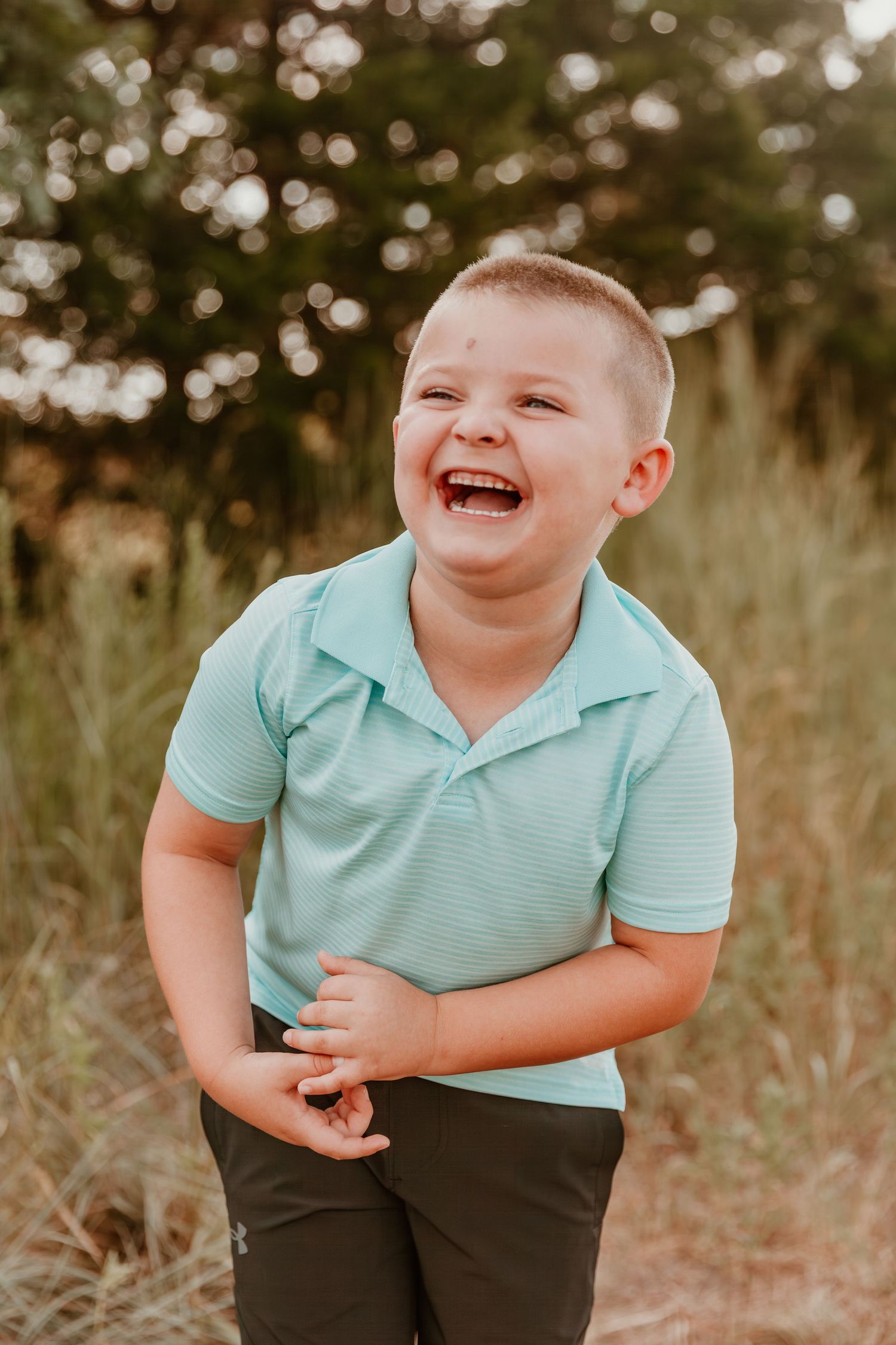 Young child in mint polo shirt laughing joyfully outdoors during golden hour.