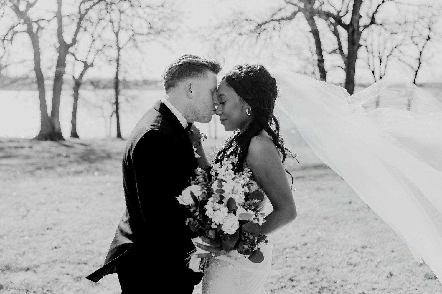 A bride and groom share a romantic moment outdoors in winter with a black and white aesthetic and beautiful floral bouquet.