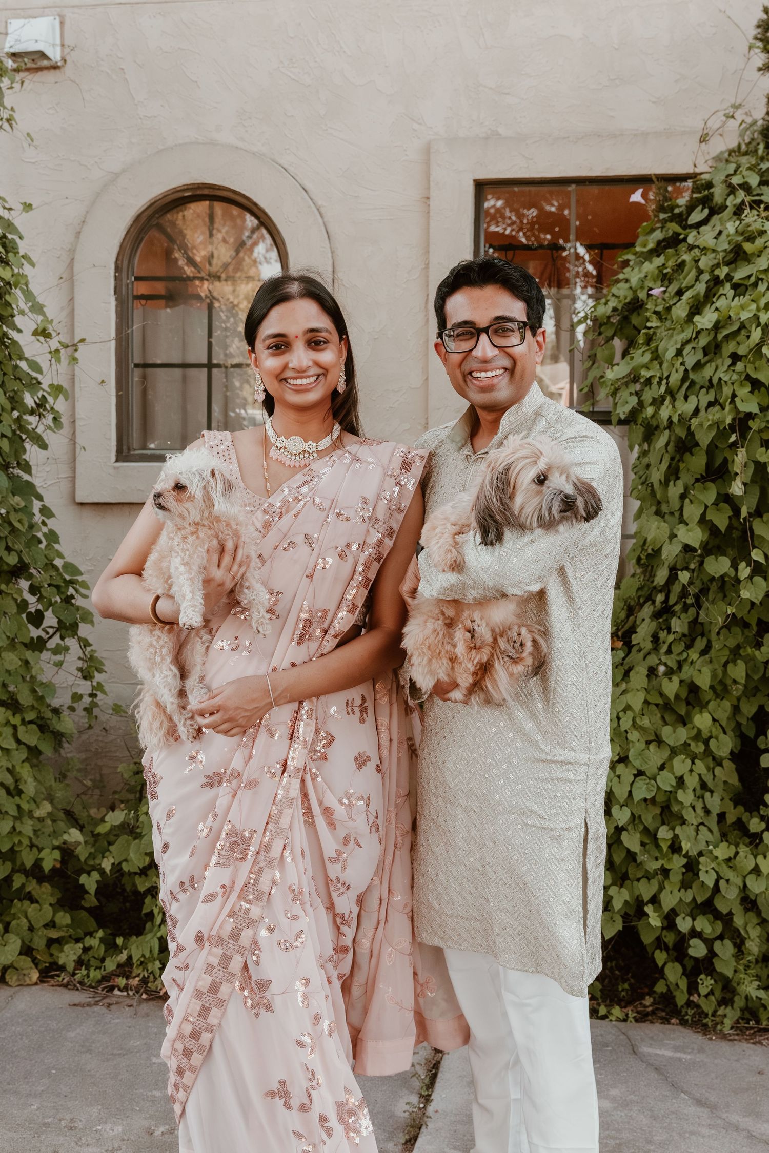 A family poses together outdoors wearing coordinating pink floral and white outfits against a white stucco wall.