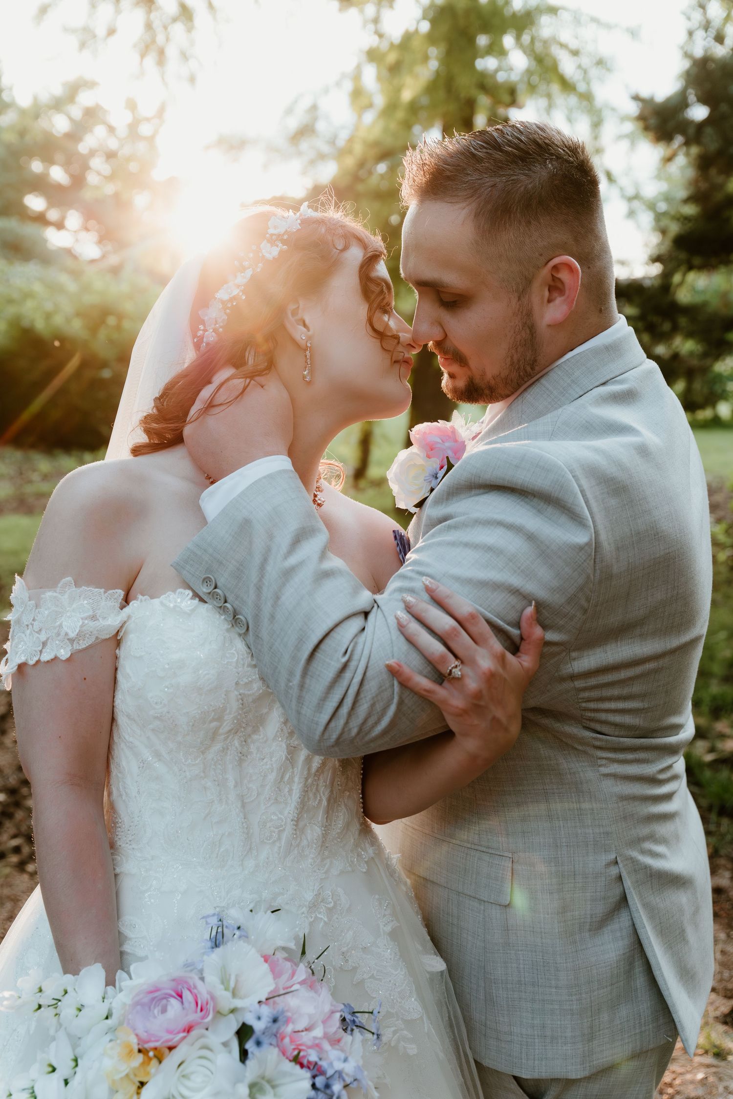 Romantic sunset wedding photo of newlyweds embracing outdoors with soft sunlight and pink floral bouquet.