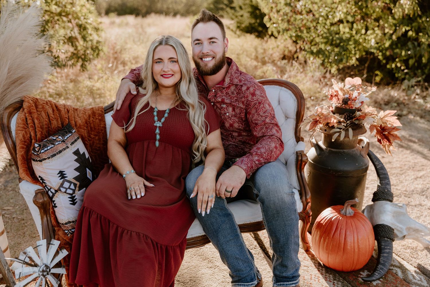 Fall-themed outdoor photo setup with burgundy dress, pumpkins and rustic wooden furniture in natural setting.