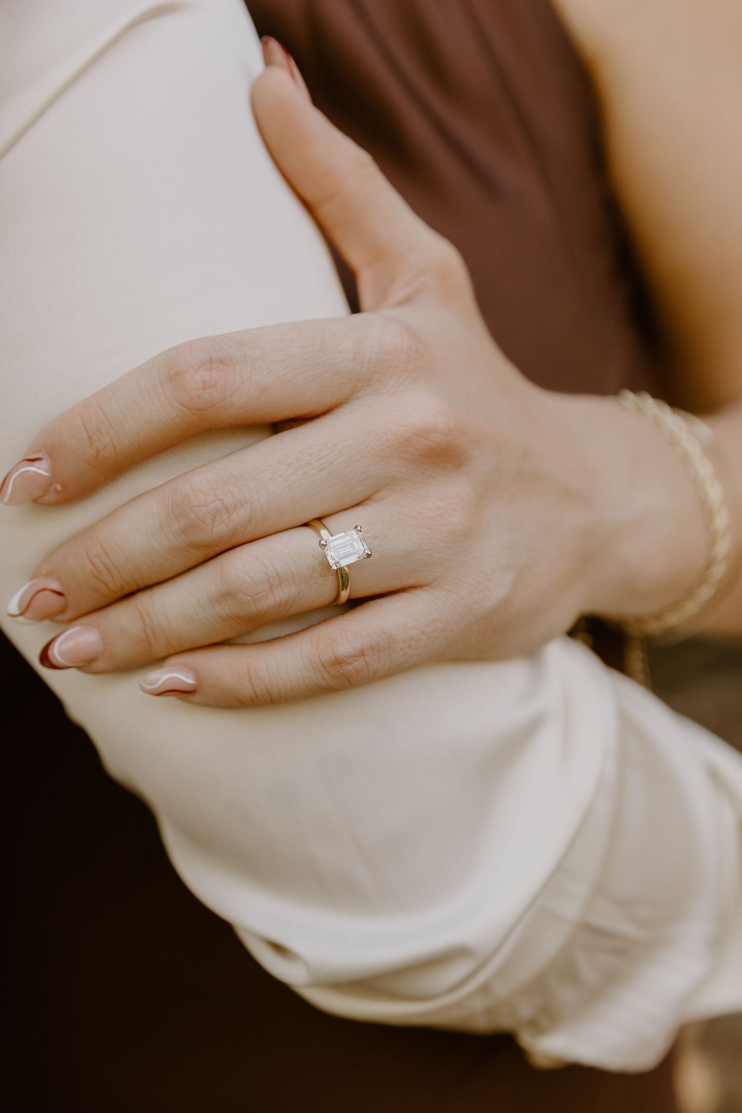 Close-up view of hands wearing an elegant engagement ring against a soft beige background.