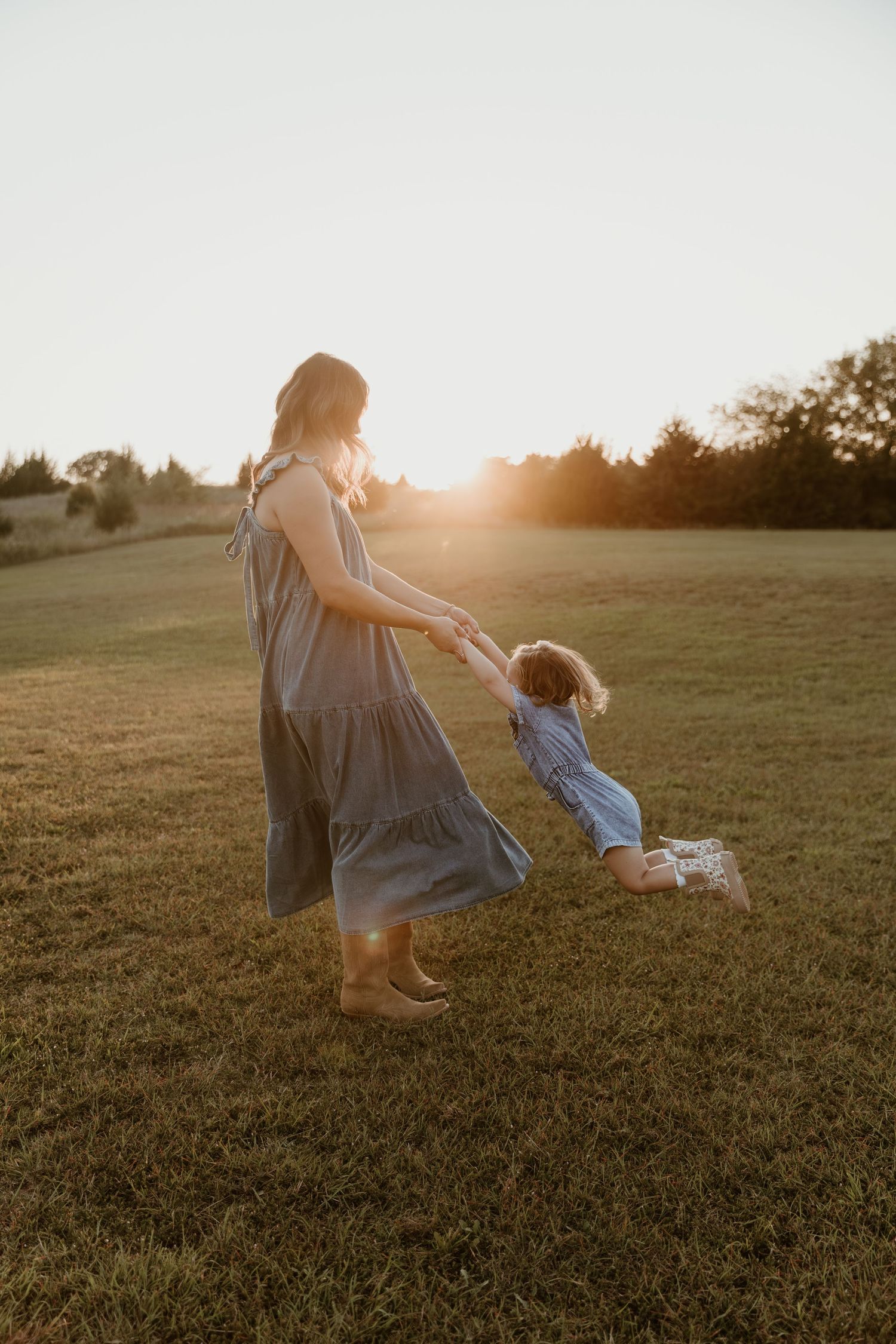 Golden sunlight illuminates a grassy field as family members play and interact during a sunset photo session.