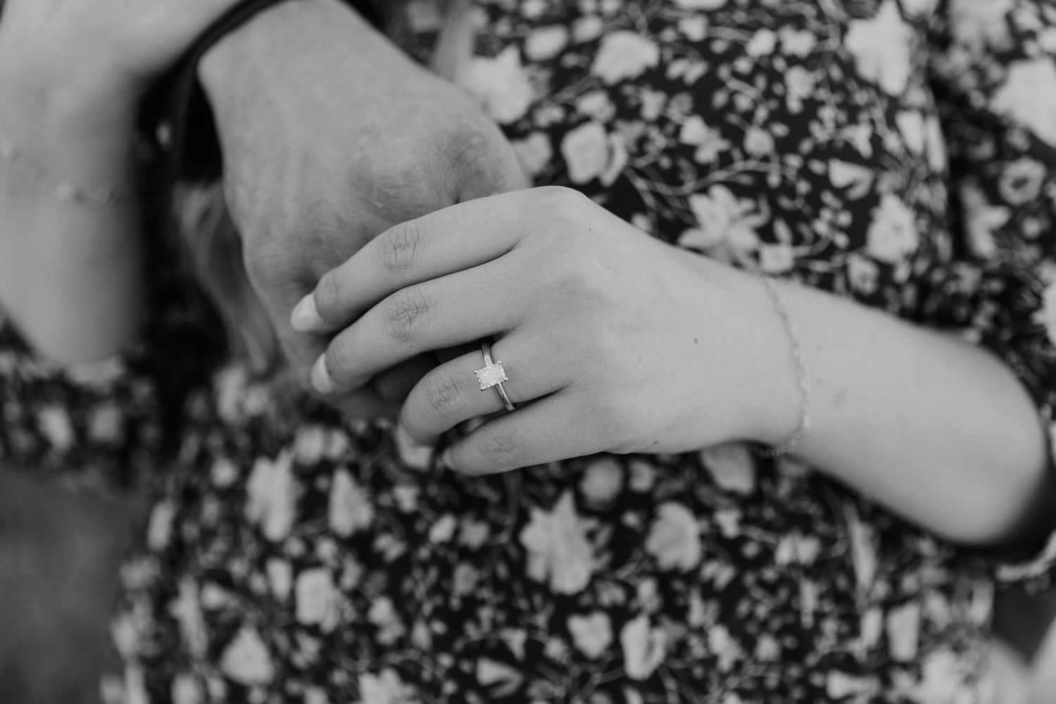Black and white close-up photo of hands holding small pebbles or stones against a textured background.