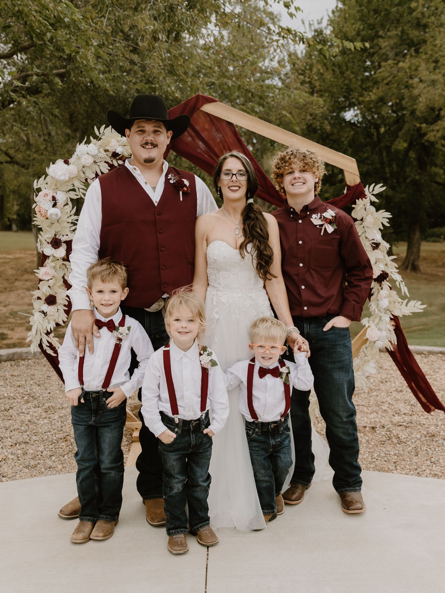 Wedding party members wearing burgundy and white attire pose playfully in an outdoor autumn setting.