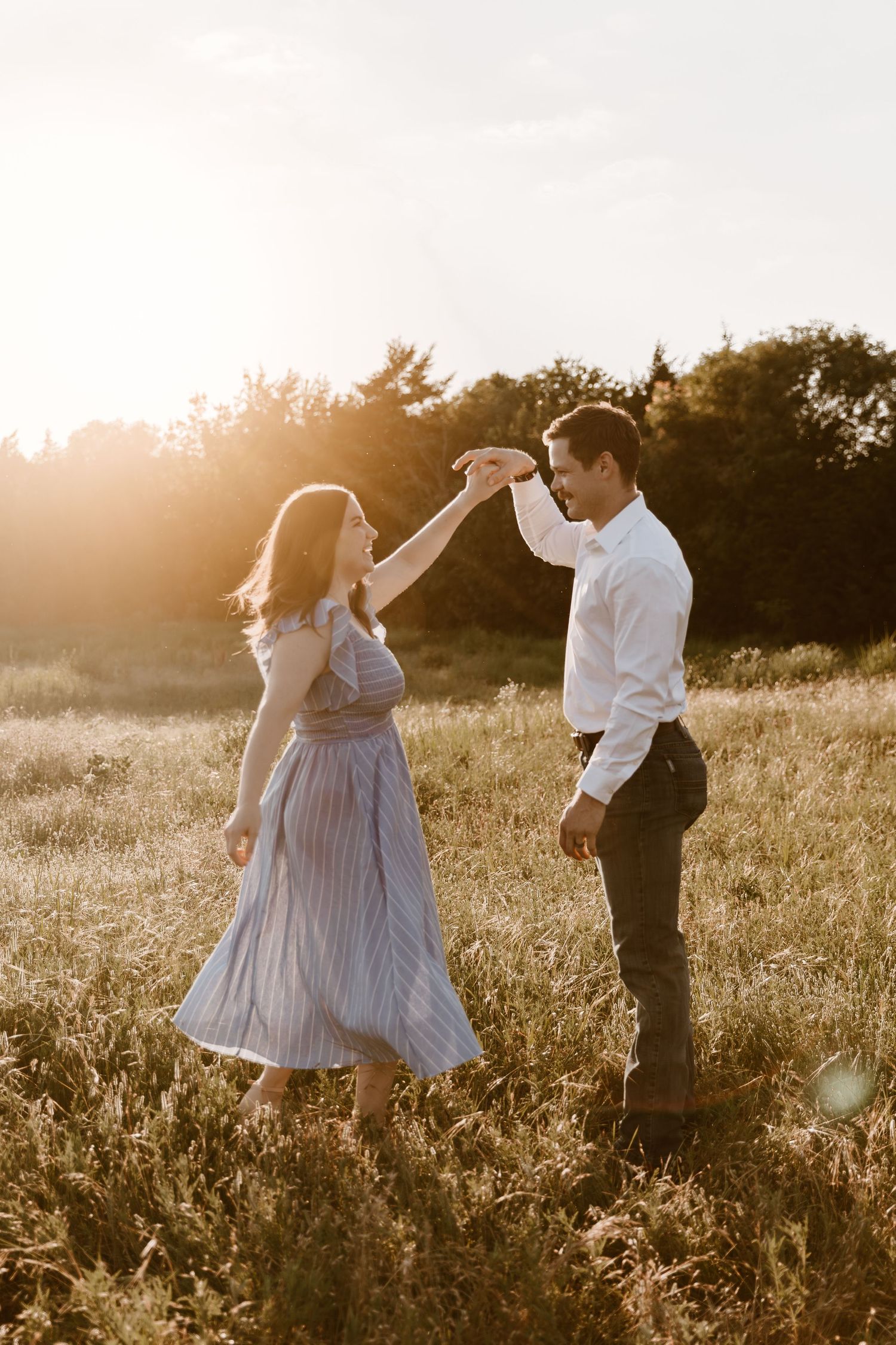 A couple dance together in a sunlit meadow at golden hour, her flowing dress swaying in the evening breeze.