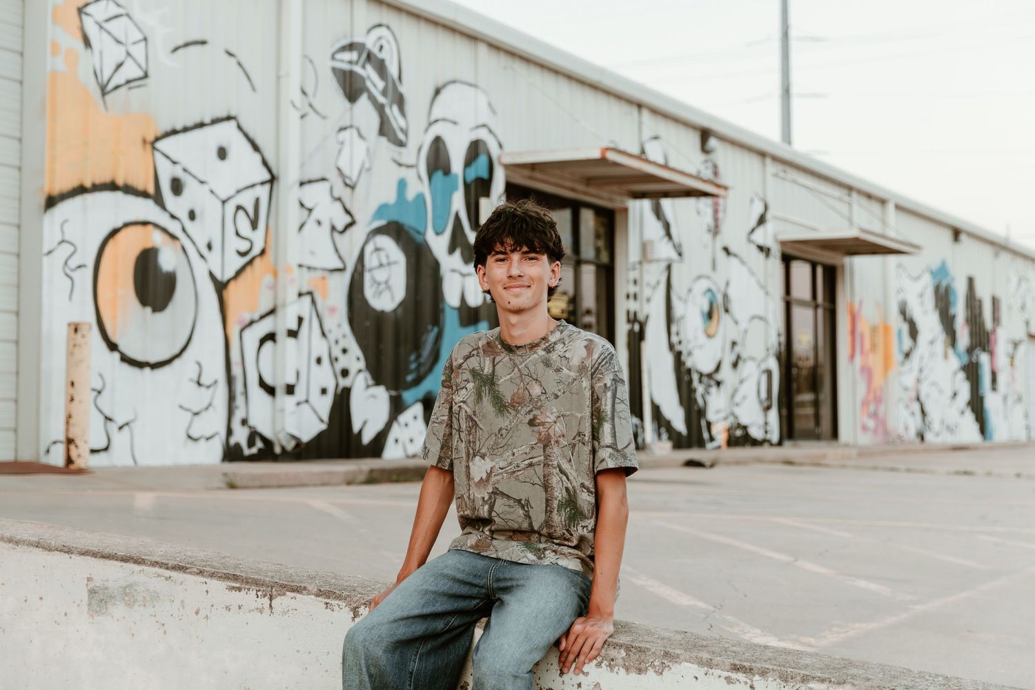A person wearing a gray t-shirt poses by a graffiti covered wall with artistic murals in black and white.