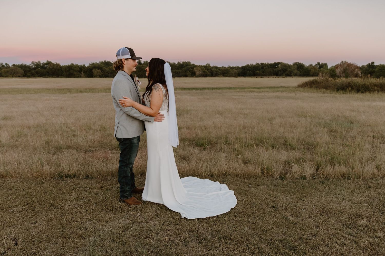 A couple shares an intimate moment in a rustic field during sunset.