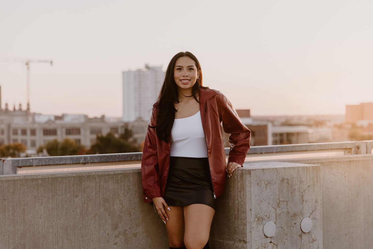 A person in a red leather jacket poses against a city backdrop during golden hour sunset.