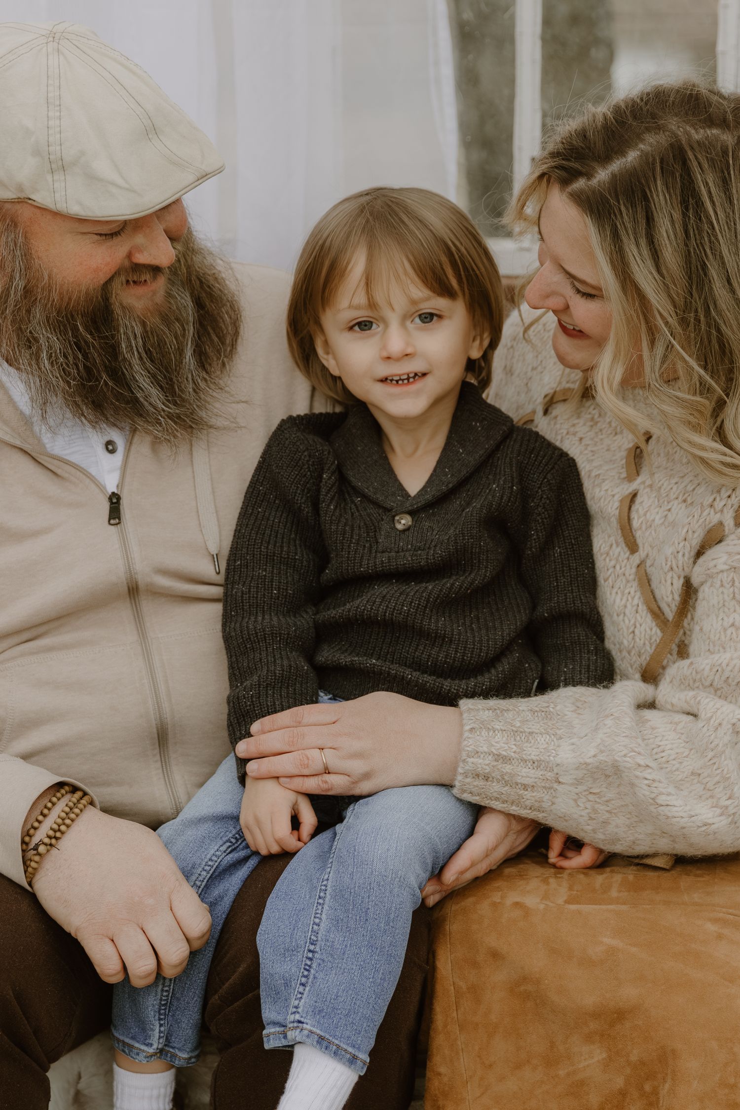 A warm family portrait in muted tones shows loving parents embracing their young child wearing a dark sweater.