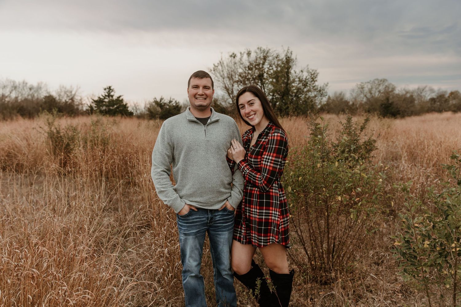 Couple in casual fall attire standing together in a golden autumn field during sunset.