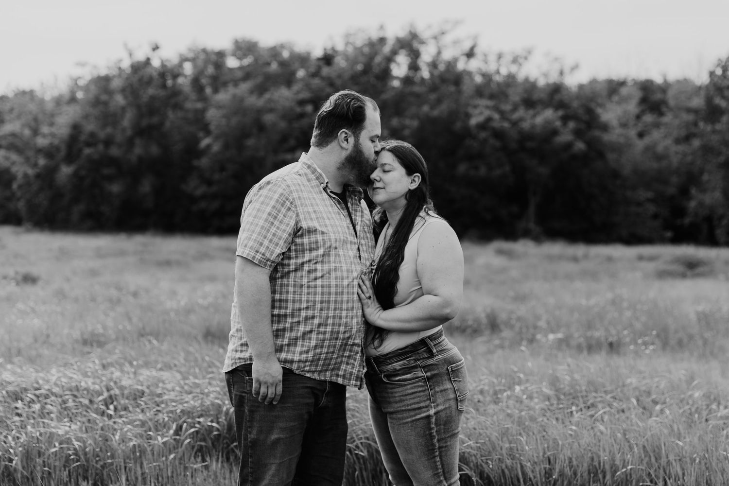 A loving couple share an intimate moment together in a black and white photo taken in a meadow.