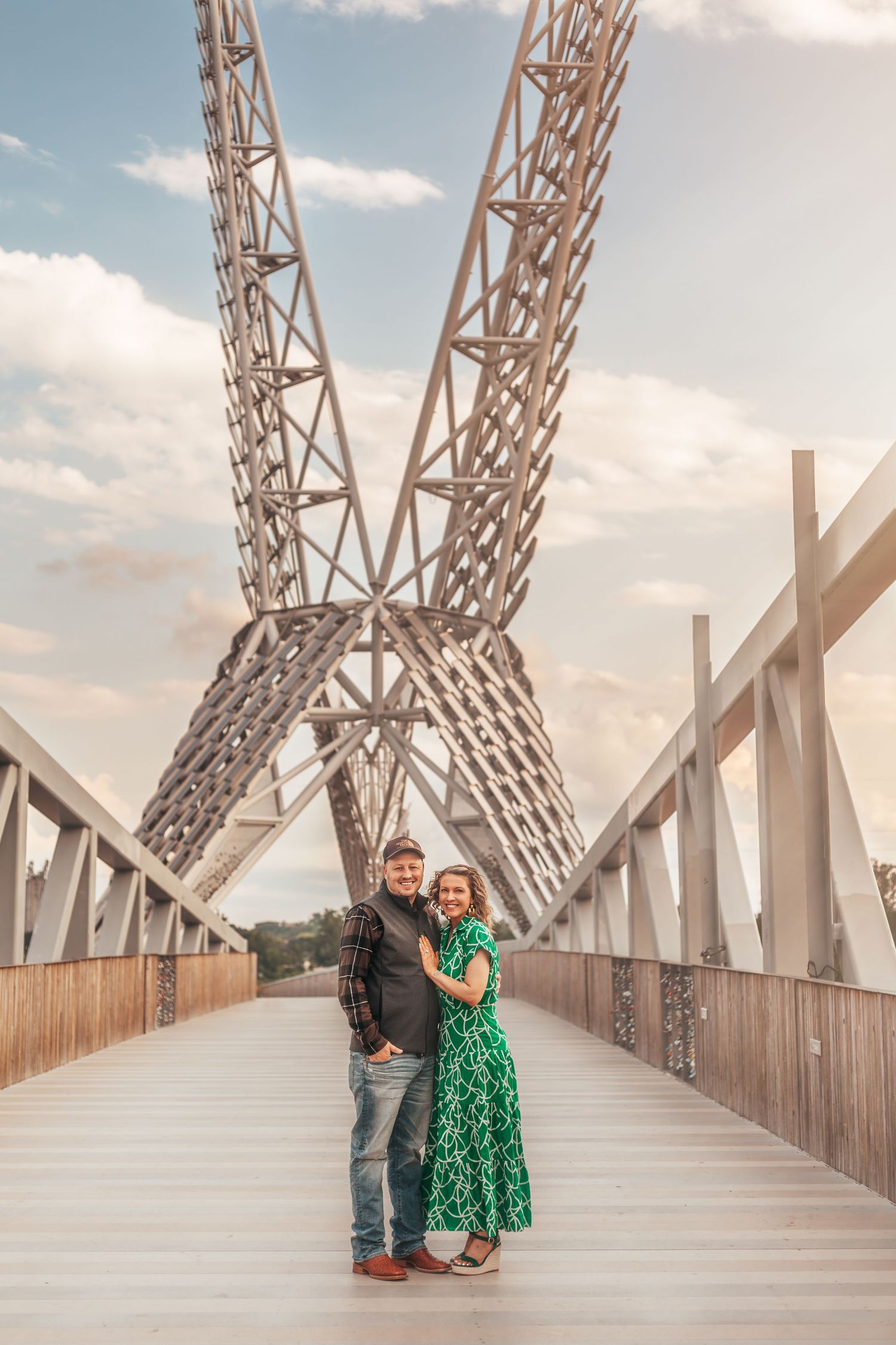 Couple standing on bridge with dramatic architectural metal structure in background.
