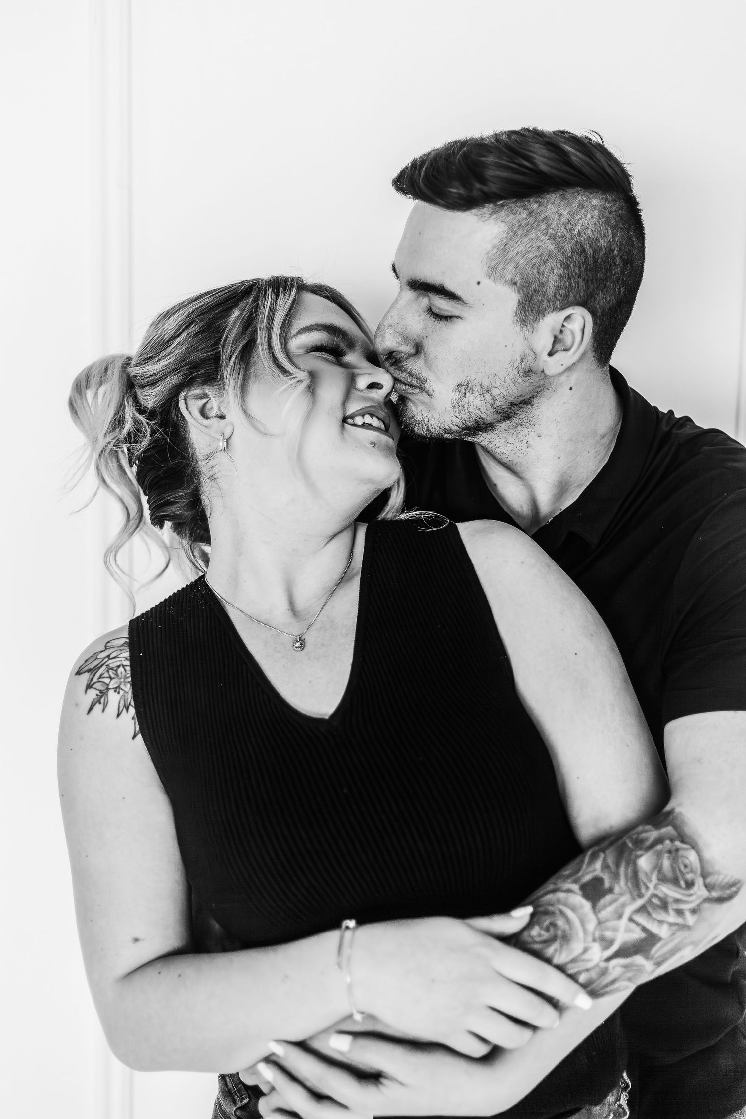 Black and white portrait of intimate couple embracing against white background.