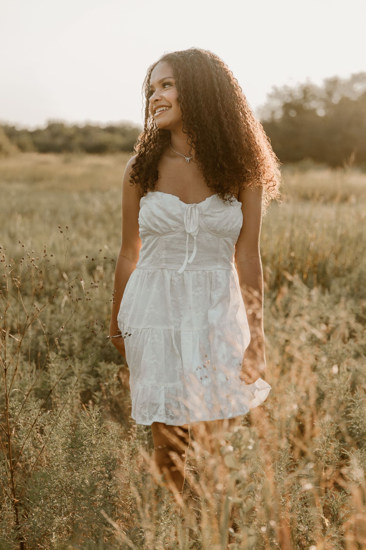 Person in a white flowy dress stands in a golden field at sunset creating a dreamy summer portrait.