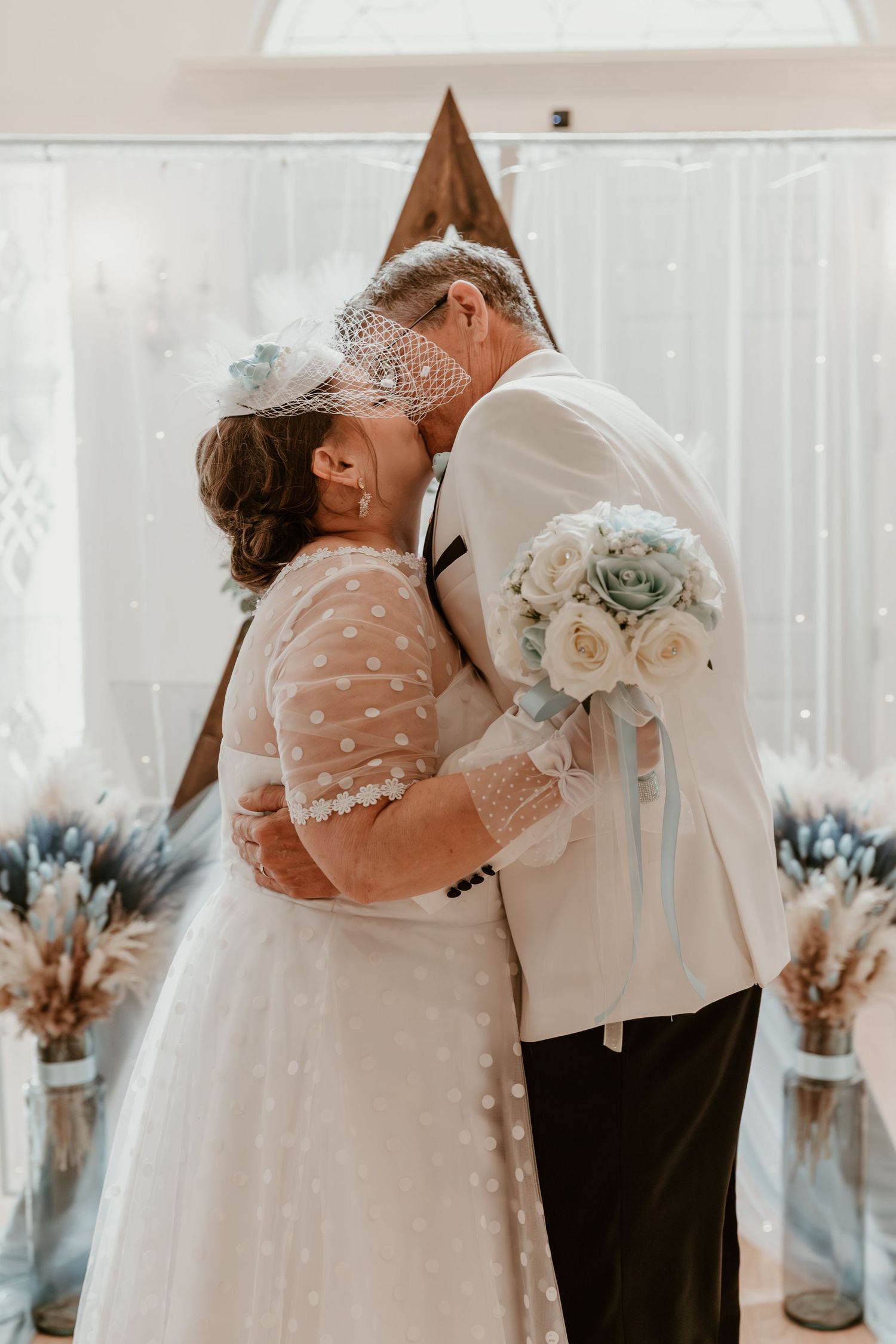 A romantic wedding moment captured in soft light with flowers and vintage decor as couple shares their first kiss.