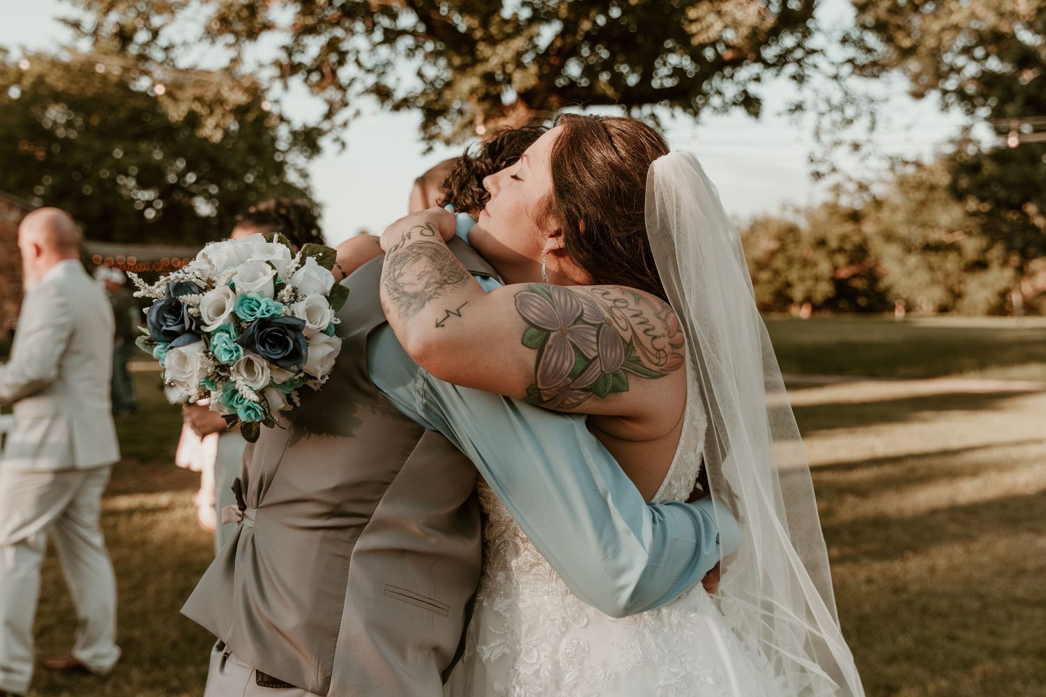 A romantic sunset wedding photo with couple embracing, illuminated by golden sunlight through trees in outdoor setting.