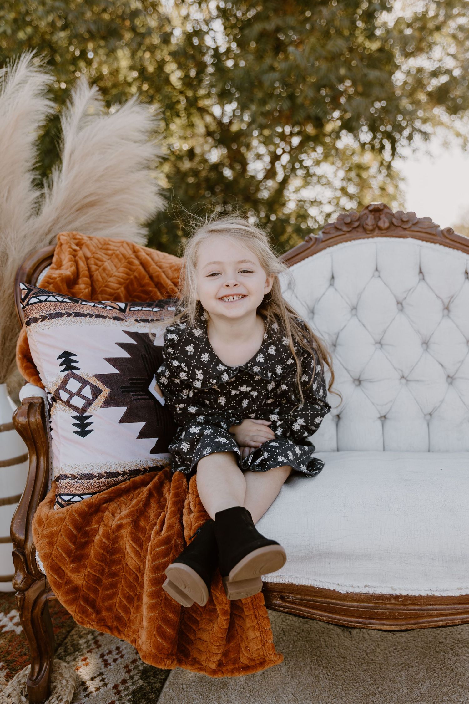Vintage white tufted sofa with southwestern style pillows and rust colored throw blanket in an outdoor setting.