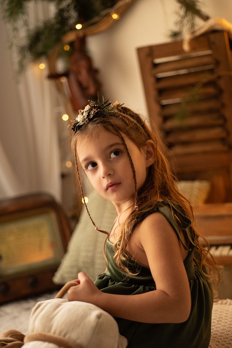 A dreamy portrait series in warm lighting shows a child in a dark green dress reclining on a beige couch.