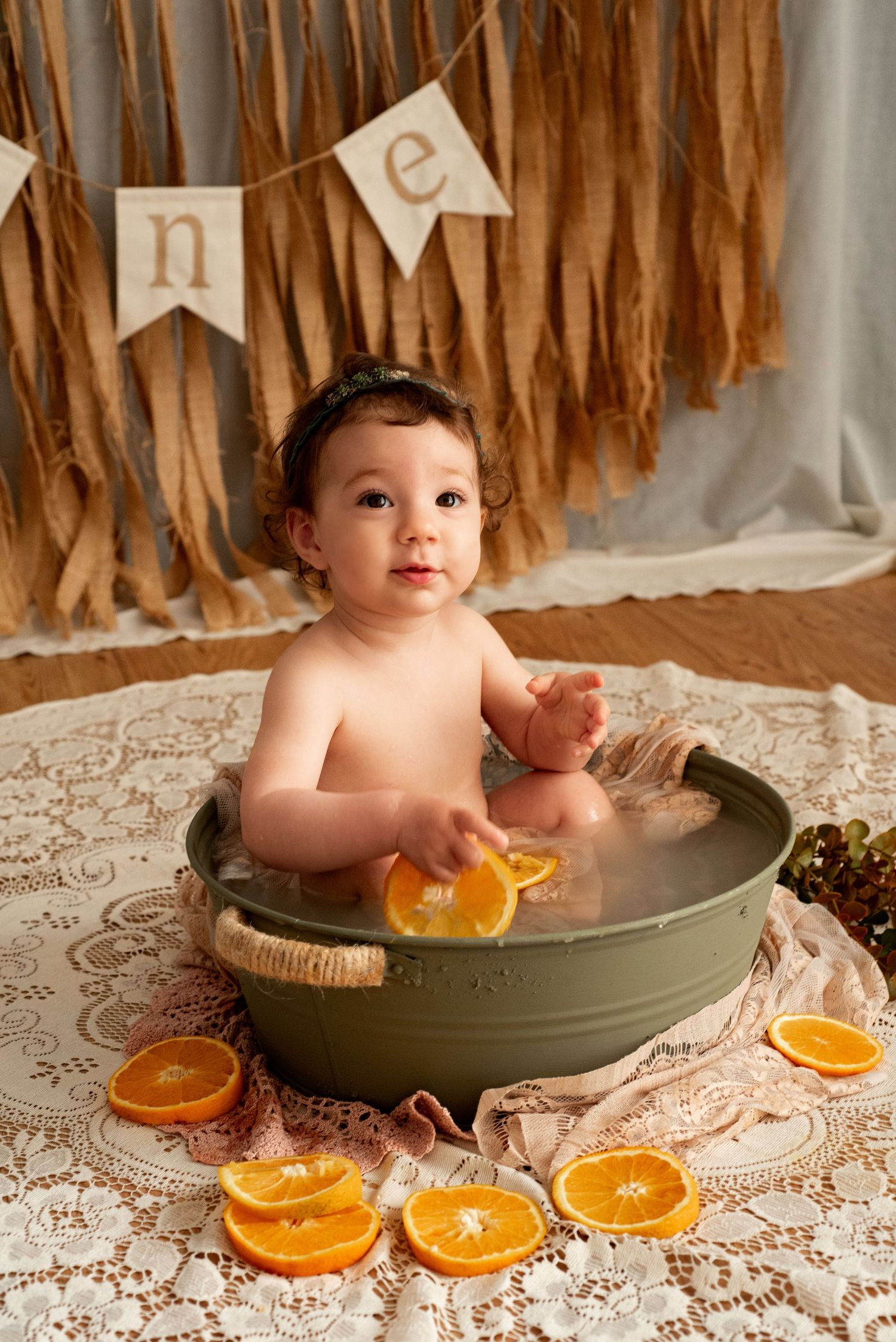 Baby taking milk bath with orange slices and lace backdrop in vintage style photography series.