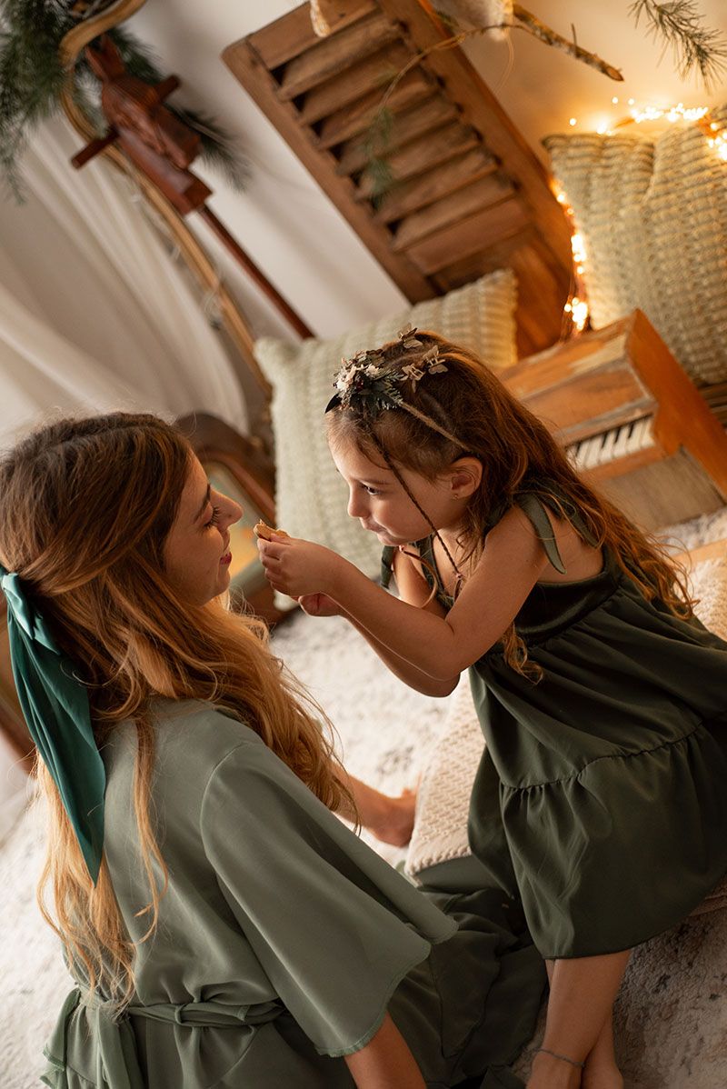 Two people in green dresses share a tender moment together in a warmly lit room with string lights.