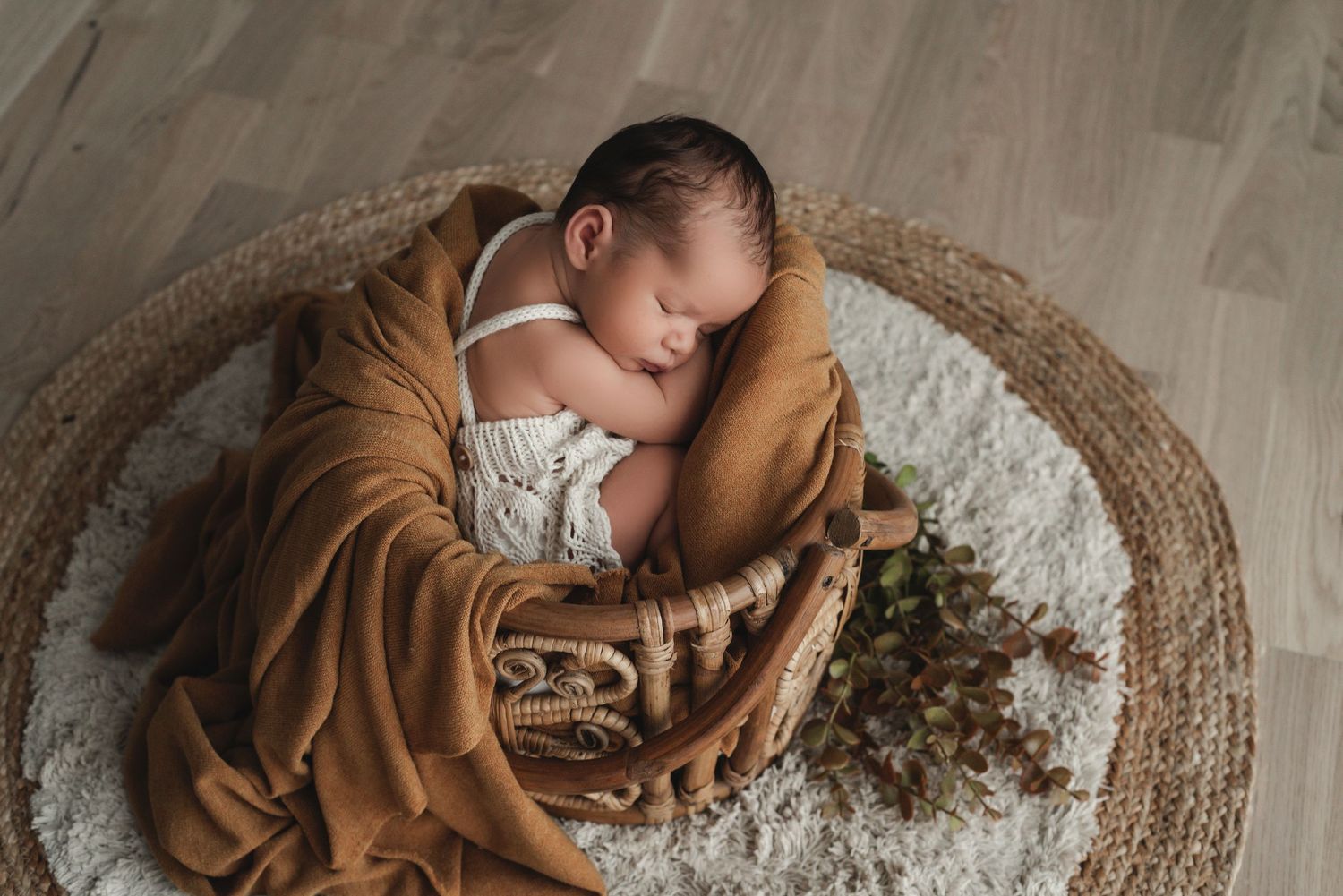Sleeping baby in brown outfit lying on round textured rug in natural light.